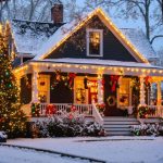 "Family home decorated with warm white and multi-colored Christmas lights at dusk with snow-dusted trees and a cozy porch."