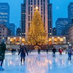 Ice skaters at Rockefeller Center on Christmas Eve beneath a towering illuminated Christmas tree, golden lights reflecting on the ice with gentle snowfall and Art Deco buildings softly blurred in the background.