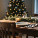 Eye-level photo of a holiday table with a single empty wooden chair beside a lit candle and simple place setting, warm golden side light, and blurred Christmas tree lights and greenery in the background, conveying remembrance and quiet hope.